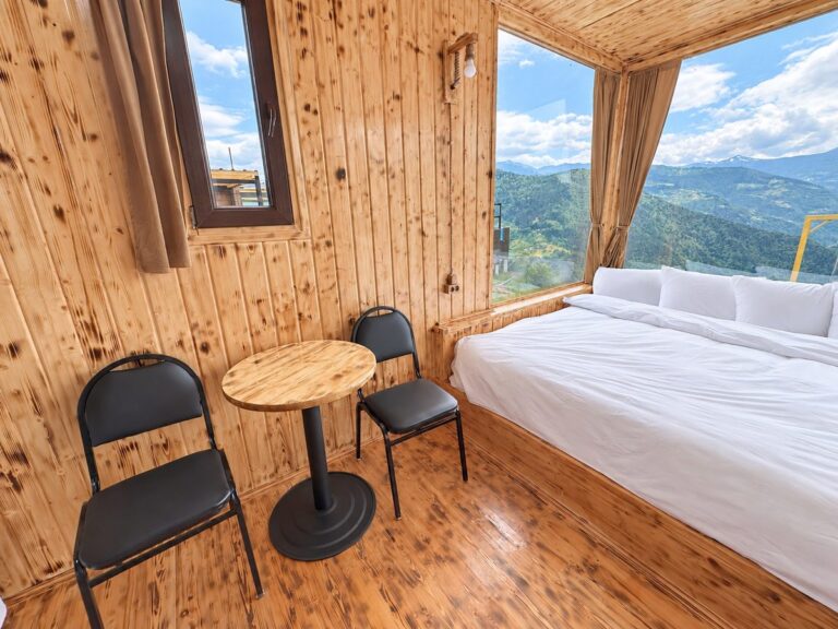 Glass cabin bedroom: bed by the panoramic window, a small table and two chairs — Nika Hotel & Club