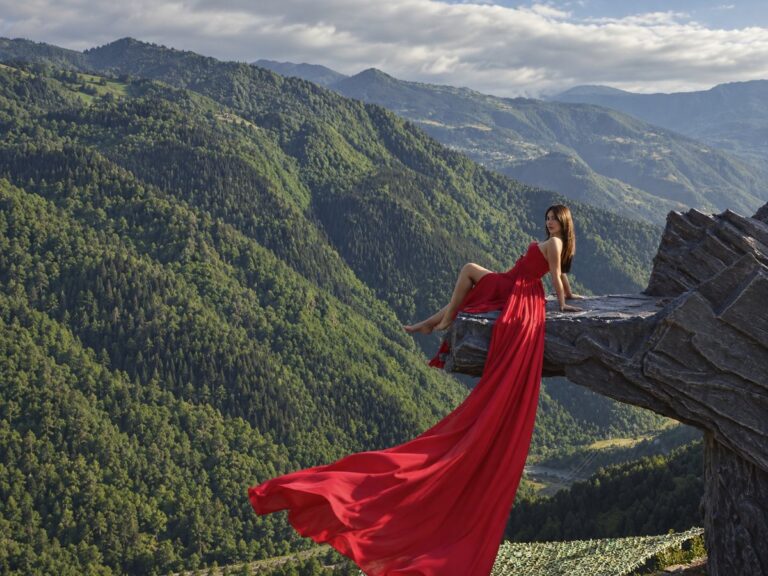 Girl in a red dress with a long flowing train on the «Rock» photo spot above the gorge in the Adjara mountains — Nika Hotel & Club
